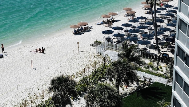 A beach with umbrellas and lounge chairs, a pool, and a building with balconies overlooking the beach. - Direct large, beachfront Condo, steps to Vanderbilt Beach, 3 bedroom, 3 bath. (Naples)
