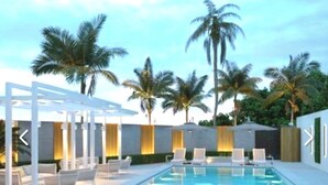 A pool area with lounge chairs, a sunbed, and palm trees. - Direct large, beachfront Condo, steps to Vanderbilt Beach, 3 bedroom, 3 bath. (Naples)
