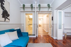 A living room with a blue sofa, a white door, and a hallway leading to a kitchen.