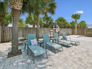 An outdoor patio area with lounge chairs, a wooden fence, and palm trees.