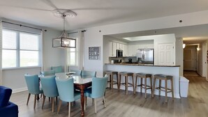 A modern kitchen with white cabinets, a stainless steel refrigerator, and a bar area with stools. - Ariel Dunes II #1310 | Gulf Views + Amazing Resort Amenities! (Miramar Beach)