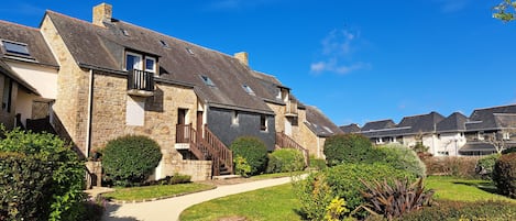 A row of stone houses with a pathway leading to the entrance, surrounded by well-maintained gardens.