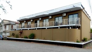 A two-story building with a balcony on the upper floor, air conditioning units, and a small garden area with plants.