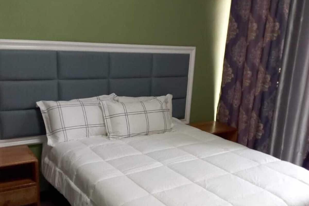 A bed with a white quilted bedspread and two pillows, a wooden nightstand, and a dark-colored rug.