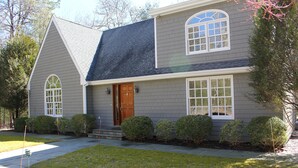 Une maison à deux étages, avec un revêtement extérieur gris, un toit foncé et une porte d’entrée dotée d’un petit porche.