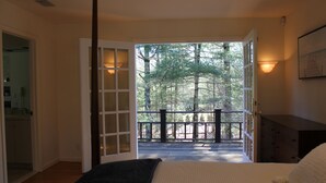 Une chambre avec une grande fenêtre, un lit, une commode et une porte donnant sur un balcon avec vue sur les arbres.