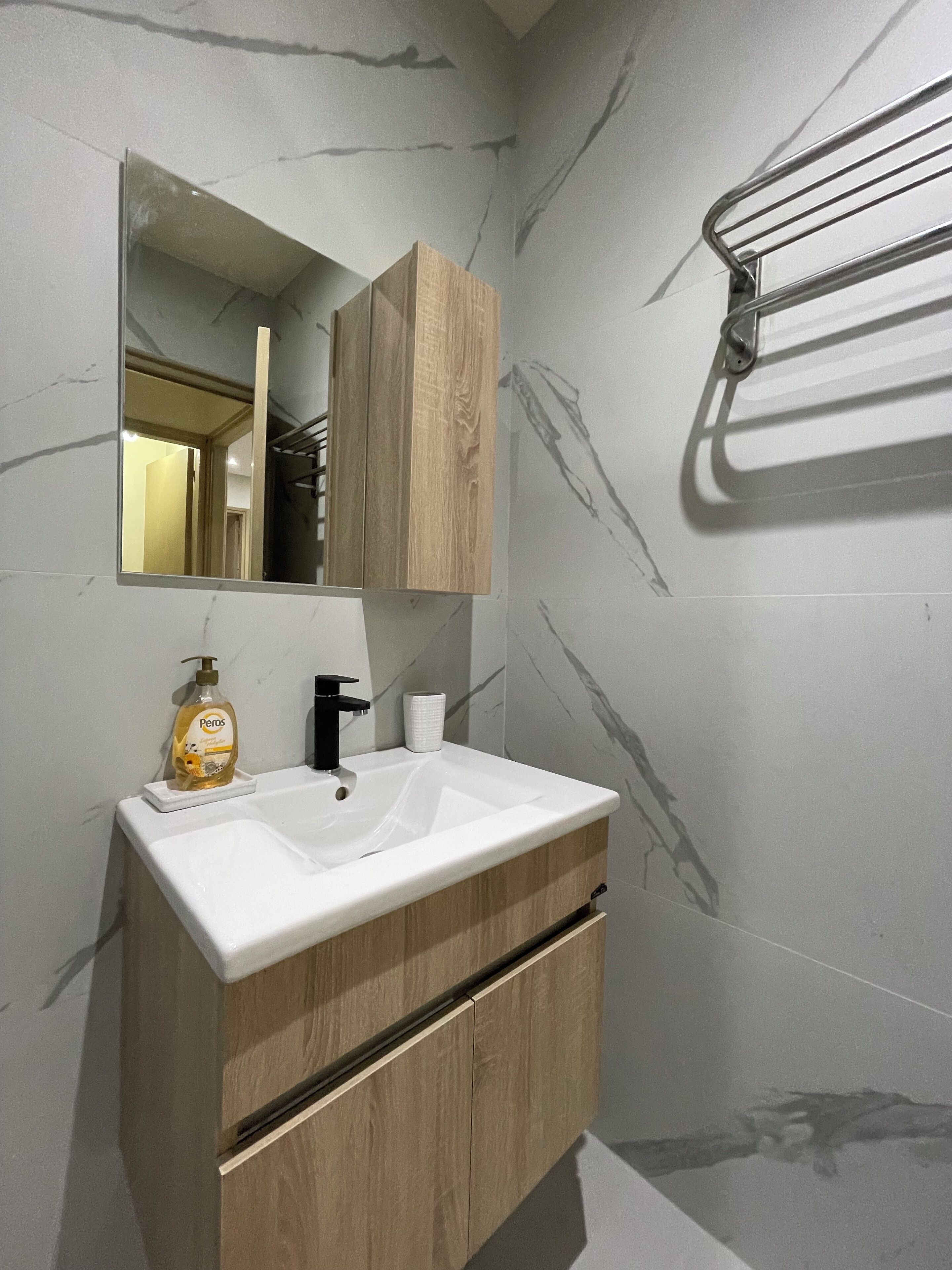 A bathroom with a white sink, wooden vanity, and a mirror.