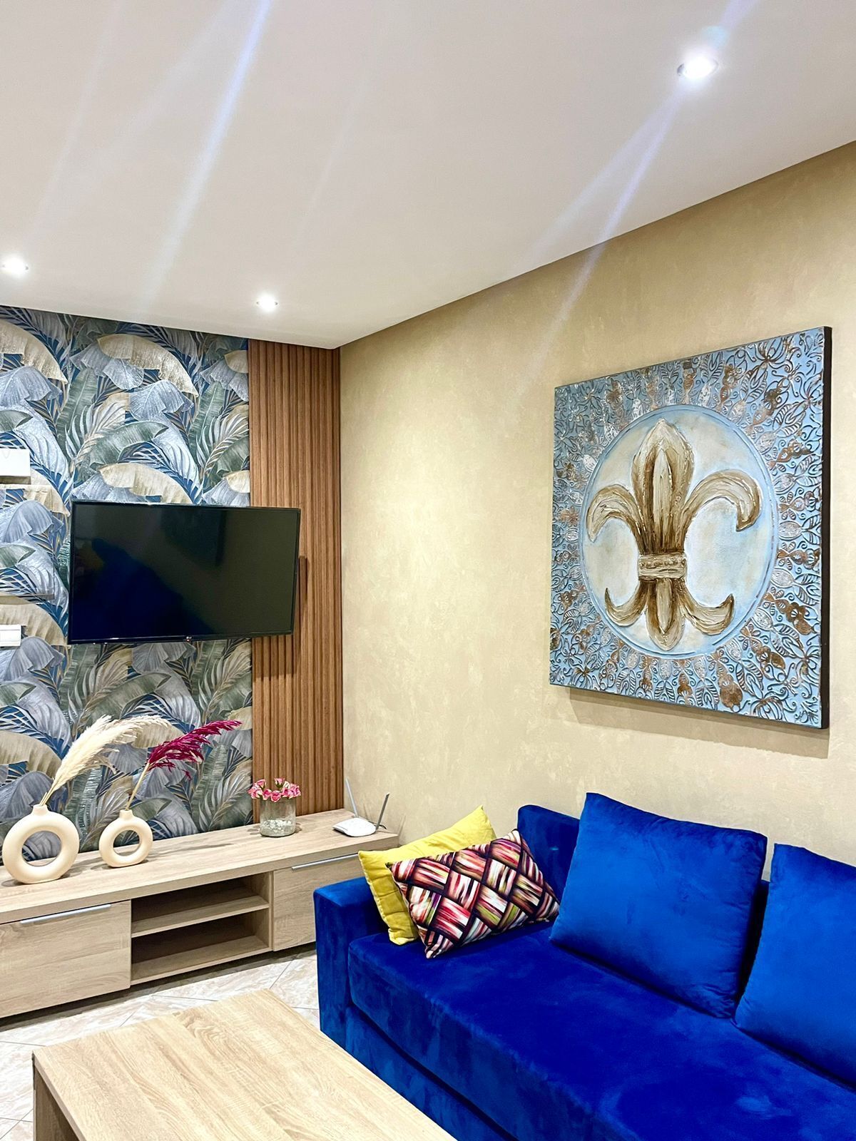Un salon moderne avec un canapé bleu, un téléviseur à écran plat, des œuvres d’art décoratives au mur et un meuble en bois.