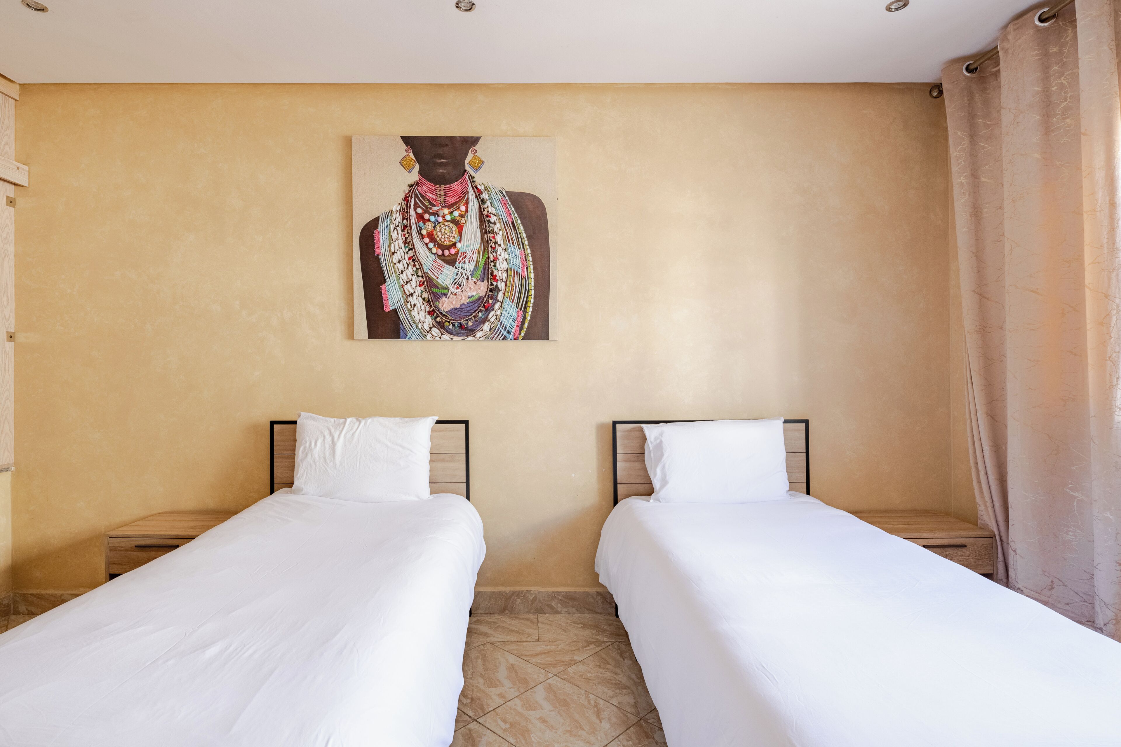 A hotel room with two single beds, a large painting on the wall, and a curtain on the window.