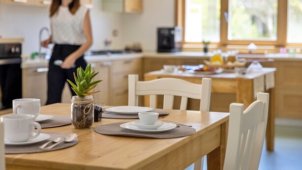 A modern kitchen with wooden cabinets, a dining table set with white plates, cups, and a small plant. - MOD SALENTO B&B - TWIN BEDROOM (Corsano)