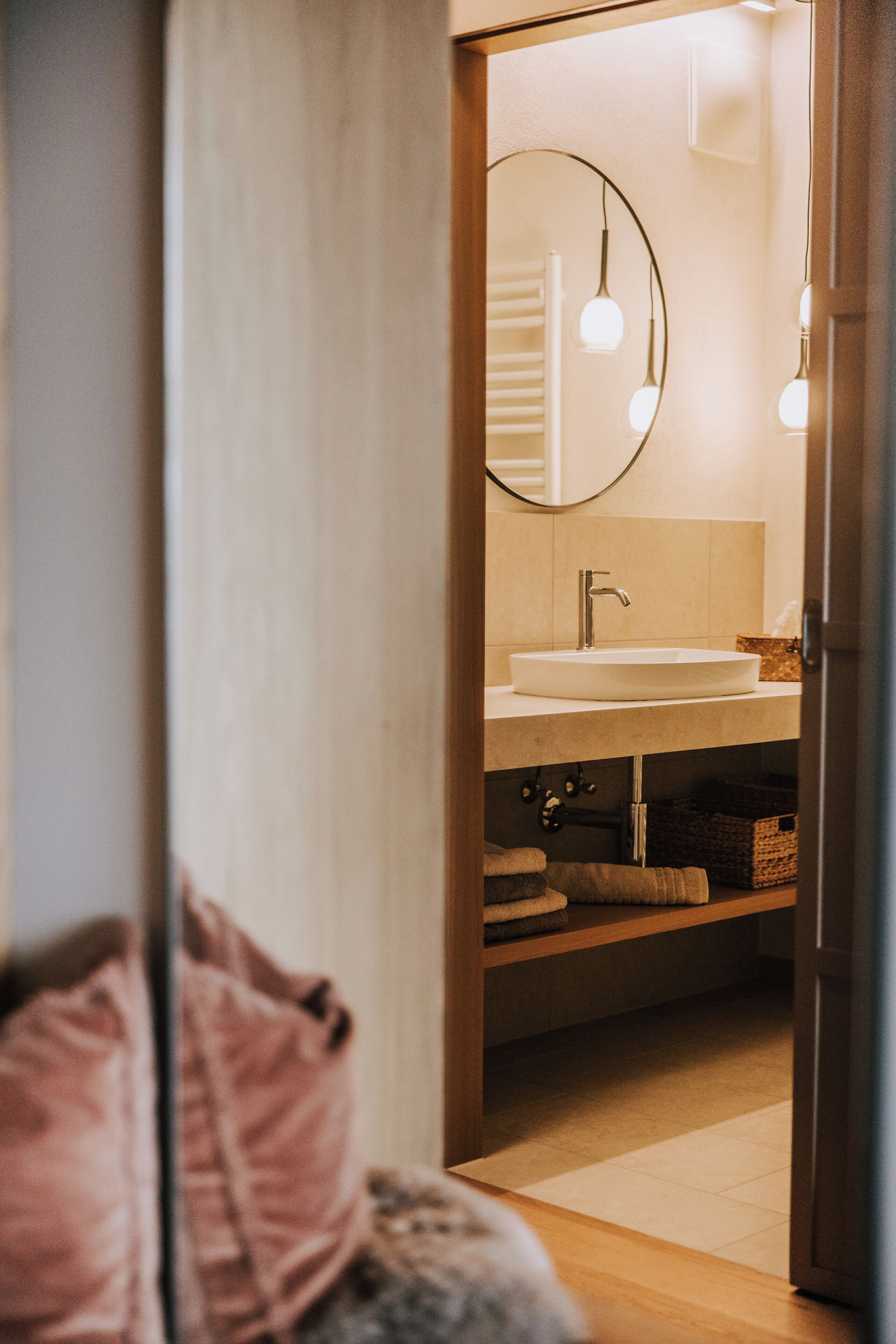 A modern bathroom with a round mirror, a white sink, and a wooden shelf.