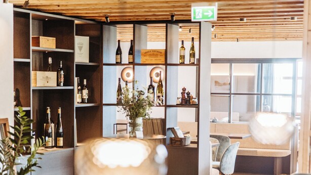 A modern interior with wooden ceiling, shelves with bottles, a table, and chairs. - Hotel Marvia (Schwarzenberg)