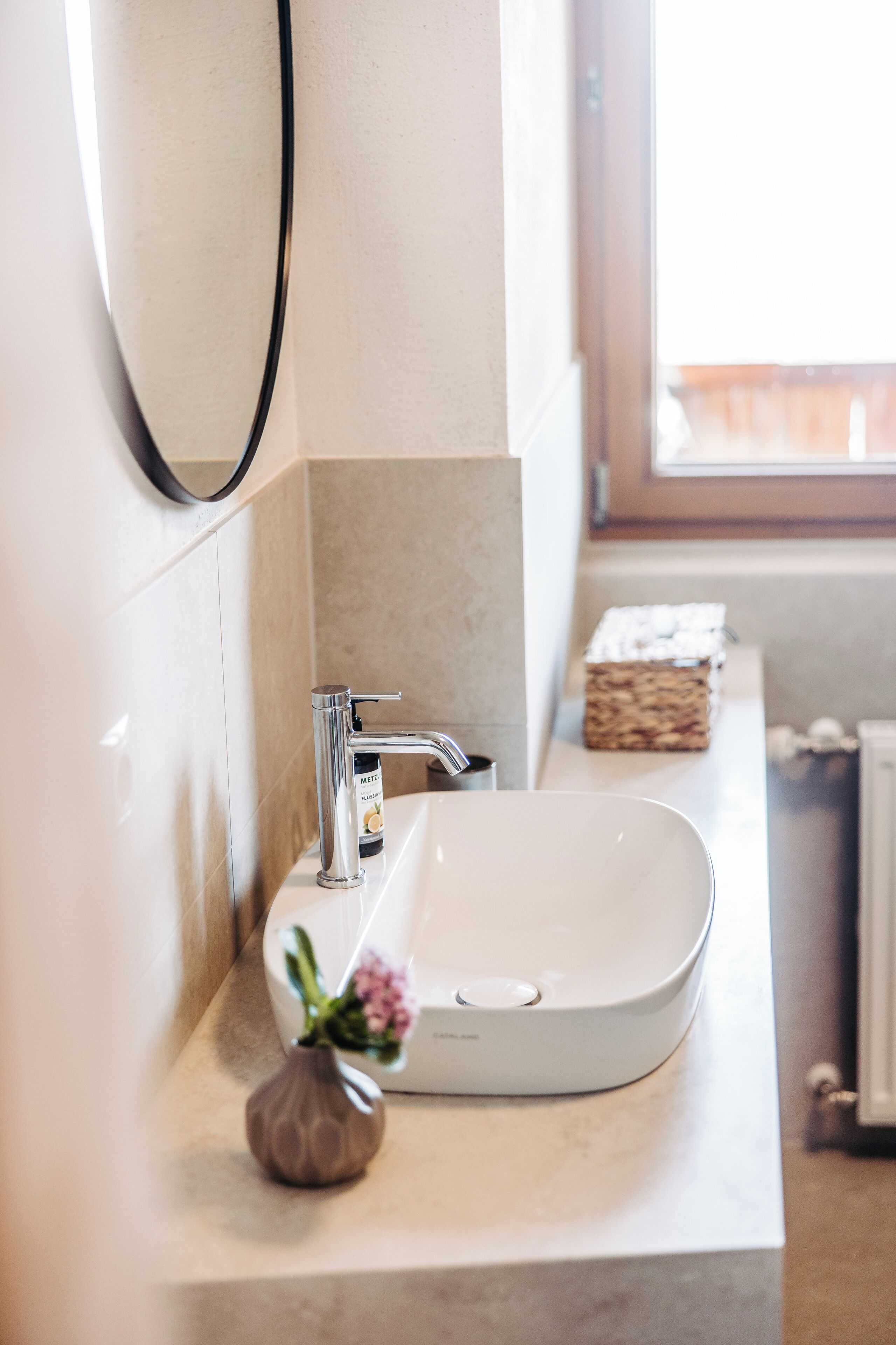 A bathroom with a white sink, a mirror, and a vase with flowers.