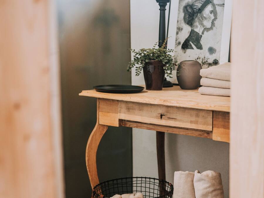 Un bureau en bois surmonté d’un plateau noir, une plante en pot, un vase et un tableau encadré. Sur le sol, on trouve deux paniers en fil de fer noirs contenant des serviettes pliées.