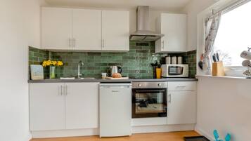 A modern kitchen with white cabinets, a green backsplash, a built-in oven, and a window with curtains.