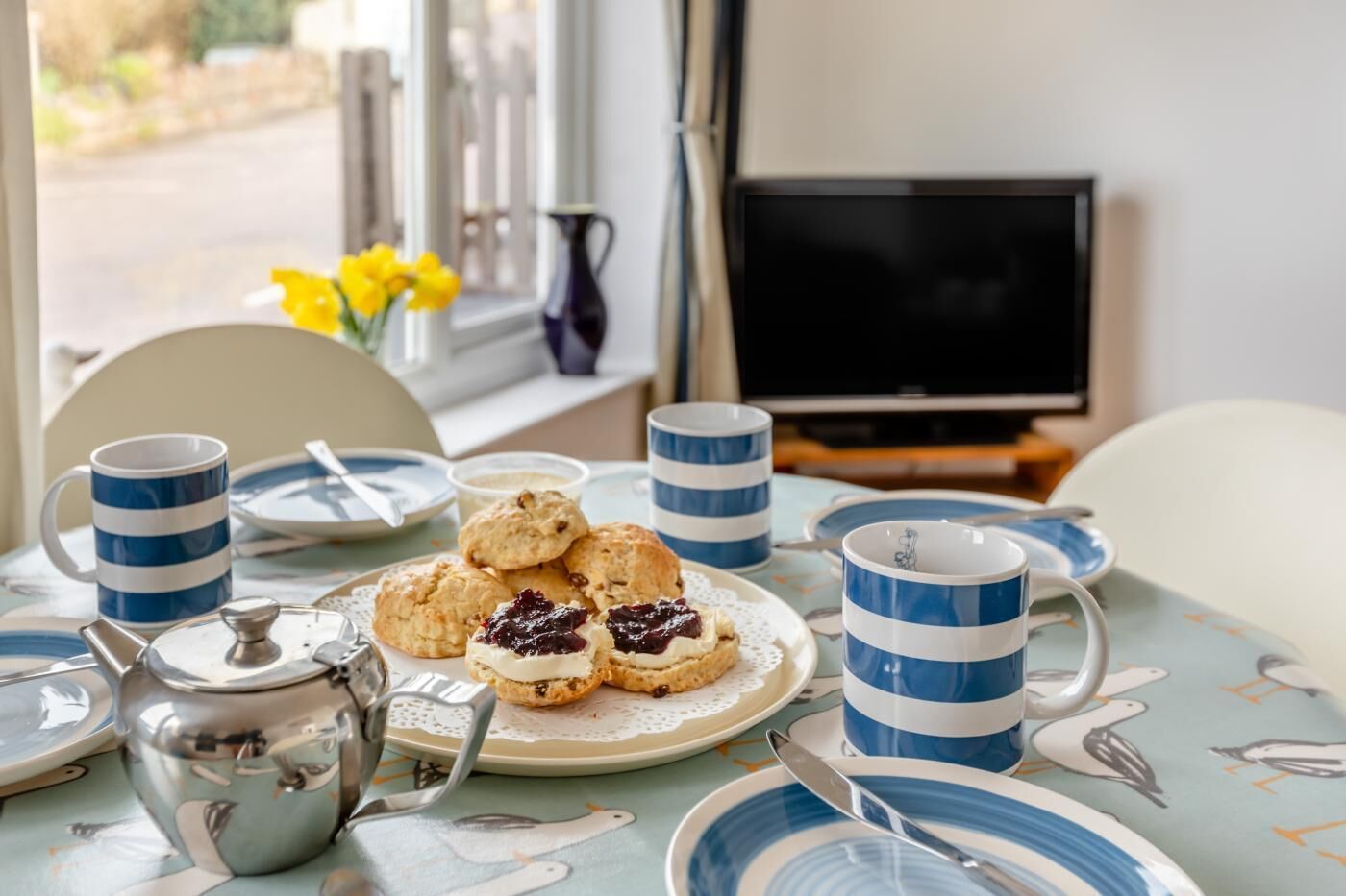 Ein Esstisch mit einer Schüssel Scones, einem Teeservice und blau gestreiften Tassen.