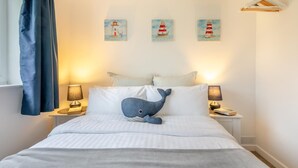 A neatly made bed with a blue whale pillow, two bedside lamps, and three paintings of lighthouses on the wall. - 2 Bed in Brixham (oc-f28884) (Brixham)