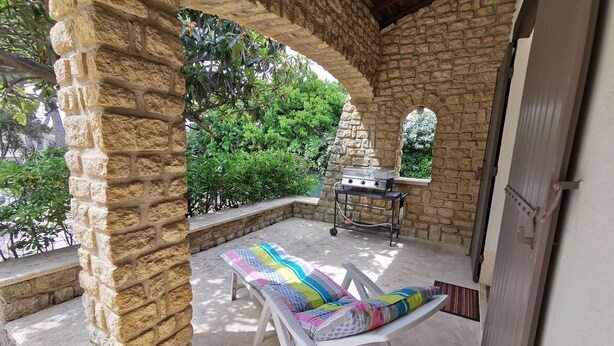 Een patio met stenen muren, een barbecue, een comfortabele loungestoel en uitzicht op groen.
