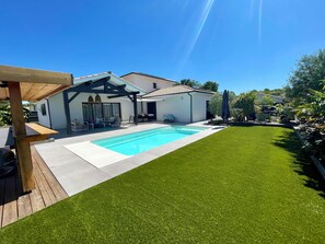 A modern house with a swimming pool, a patio with outdoor furniture, and a well-maintained lawn.