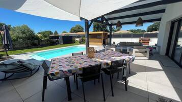An outdoor patio with a pool, a covered dining area, and a barbecue setup.