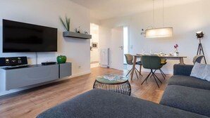 Un saló modern amb televisió de pantalla plana, sofà gris, taula de dinar i una taula rodona petita amb revistes.