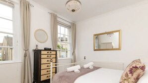 Ein Schlafzimmer mit Bett, Kommode, Spiegel und einem Fenster mit Vorhängen.