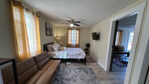 Ein Schlafzimmer mit Bett, Sofa, Deckenventilator, Fernseher und Blick ins Freie.