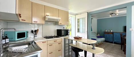 A compact kitchen with a microwave, stove, and sink. There is a small dining area with a table and chairs.