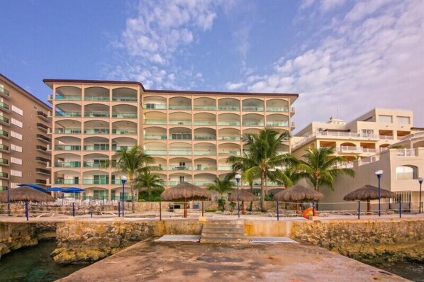 Un hotel de varios pisos con balcones, palmeras y una fuente en primer plano.