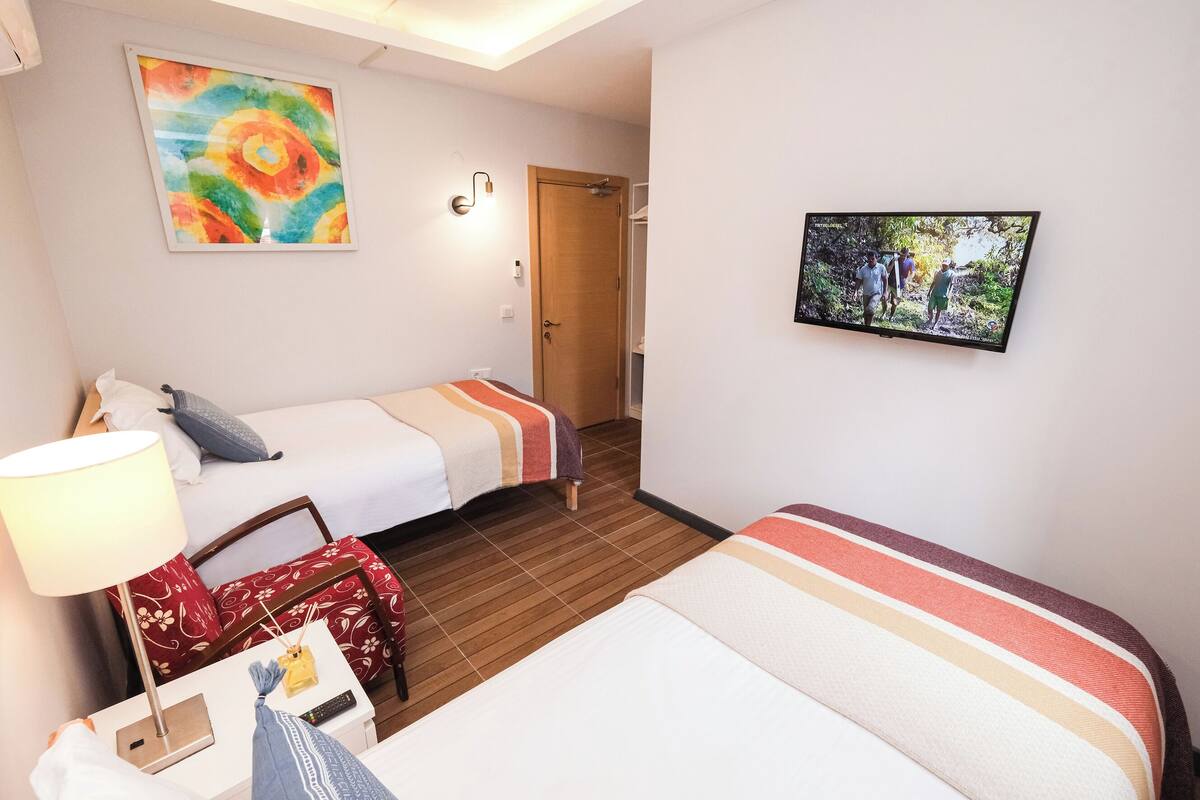 A hotel room with two beds, a TV, a painting, and a wooden floor.
