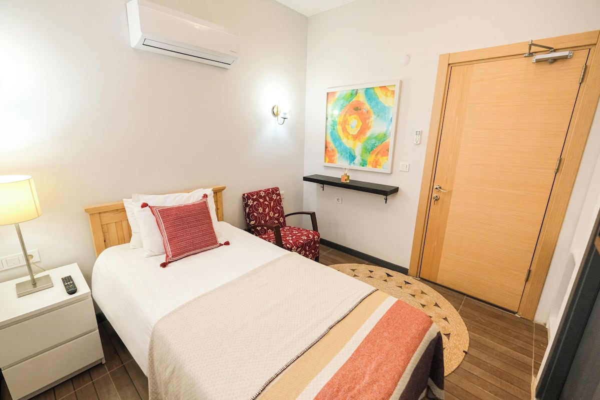 A neatly arranged bedroom with a bed, bedside table, chair, and a door.