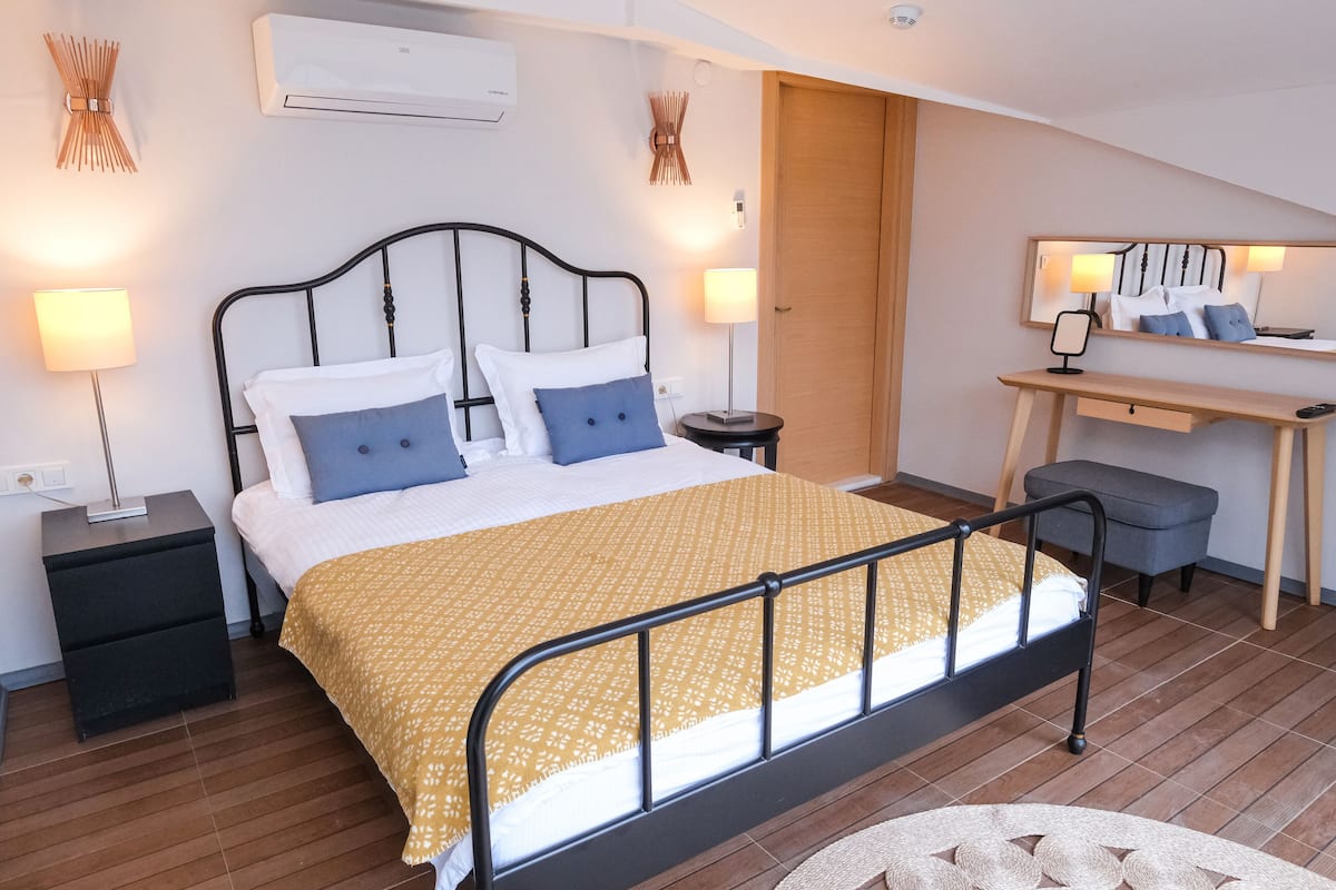 A bedroom with a bed, bedside tables, a desk, a chair, and a round table.