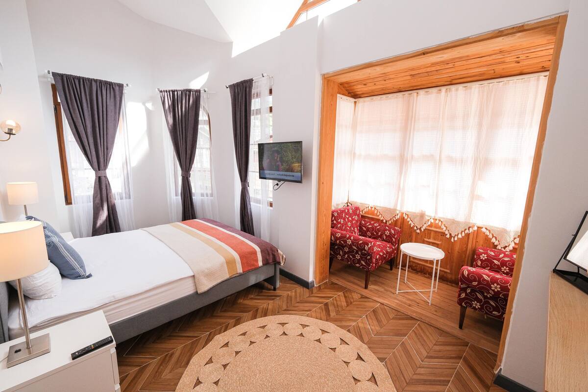 A hotel room with a bed, a TV, a sofa set, and a wooden herringbone floor.
