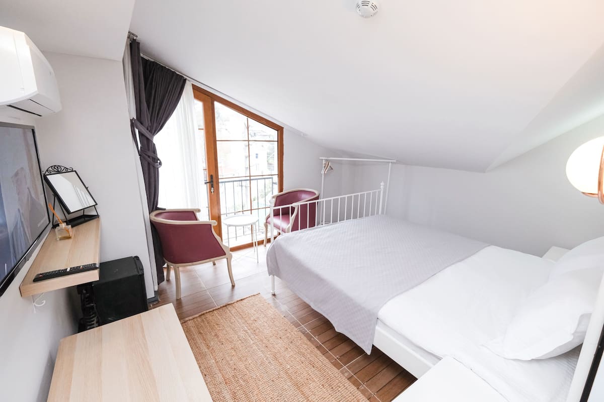 A bedroom with a bed, a desk with a computer, a chair, and a window with curtains.