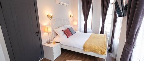 Quarto com cama, mesas de cabeceira, ar-condicionado, cortinas e televisão.
