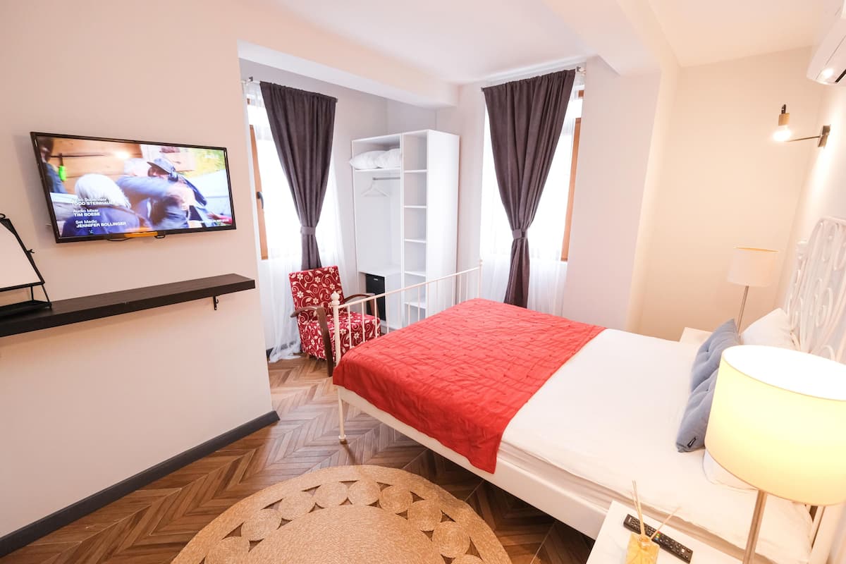 A hotel room with a bed, a TV mounted on the wall, a wardrobe, and a chair.