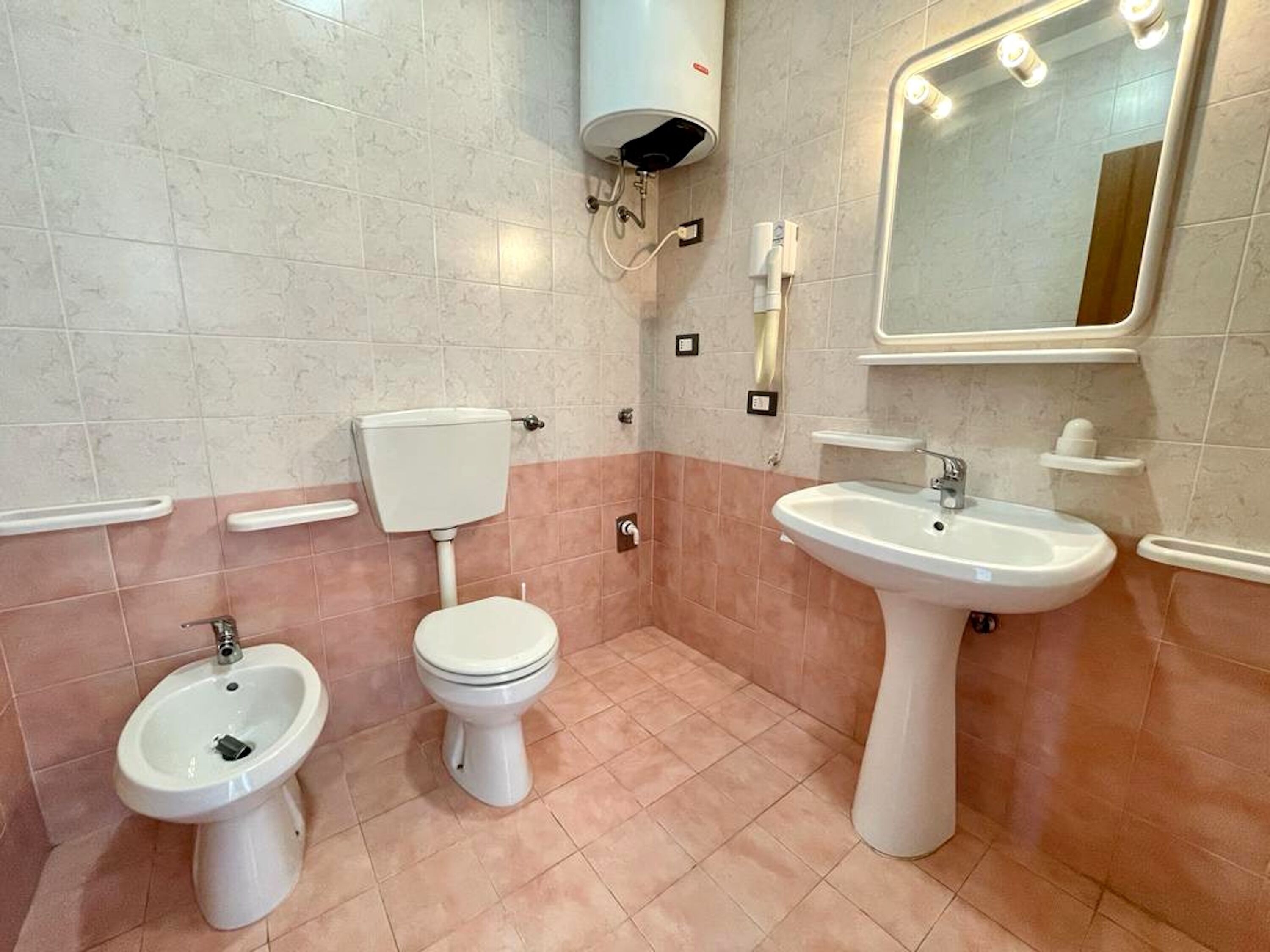 A bathroom with a toilet, bidet, and sink, all in white.