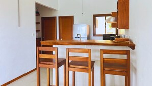 Een keuken met een houten aanrecht, drie houten stoelen en een koelkast.