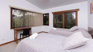 Een slaapkamer met twee bedden, een bureau en een raam met jaloezieën.