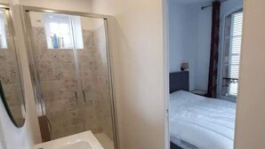 A compact bedroom with a bed, a small bedside table, and a window with curtains. - Cabourg Plein Centre - Appartement Douillet et Lumineux (Cabourg)