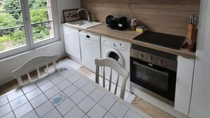 A compact kitchen with white cabinets, a microwave, a sink, a washing machine, and a dining table with chairs. - Cabourg Plein Centre - Appartement Douillet et Lumineux (Cabourg)