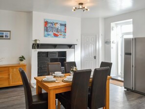 Een eethoek met een houten tafel en stoelen, een schilderij erboven en een moderne keuken op de achtergrond.