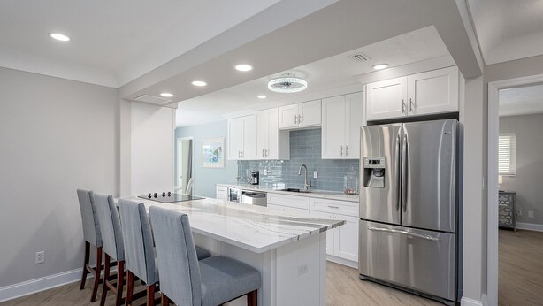 A modern kitchen with a central island, stainless steel appliances, and a light blue backsplash.