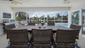 A dining area with a pool view, wicker furniture, ceiling fans, and a grill.