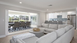A modern living room with a grey sectional sofa, a coffee table, and a dining area with wicker chairs.