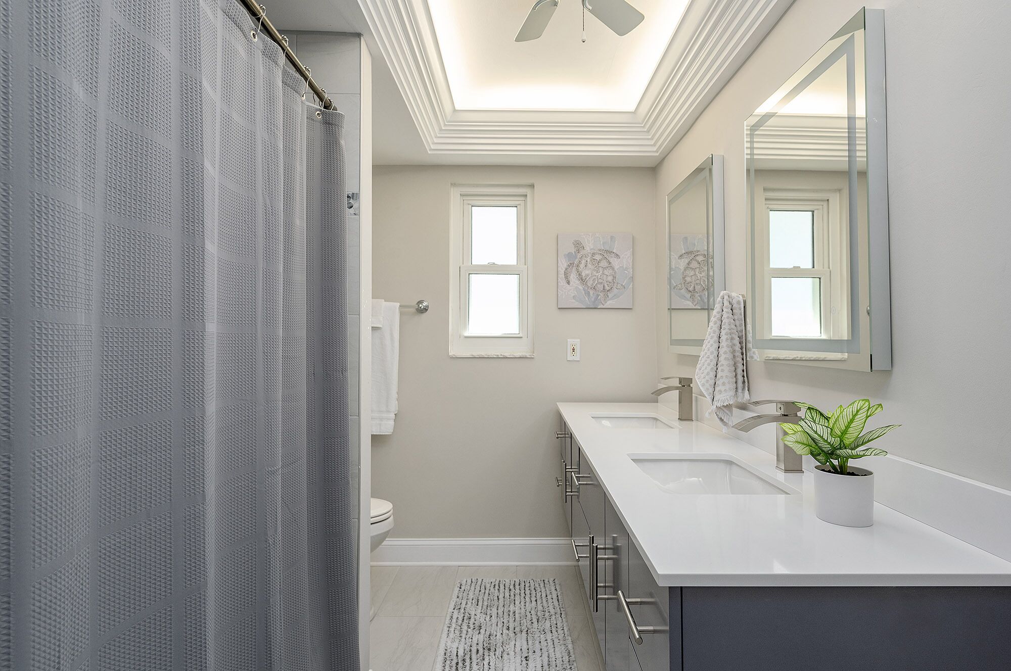 A modern bathroom with a shower curtain, a toilet, a sink with a mirror, and a ceiling fan.