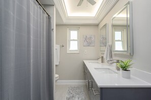 Un baño moderno con cortina de ducha, inodoro, lavamanos con espejo y ventilador de techo.