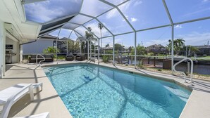 A clear pool with a covered area, lounge chairs, and a grill.