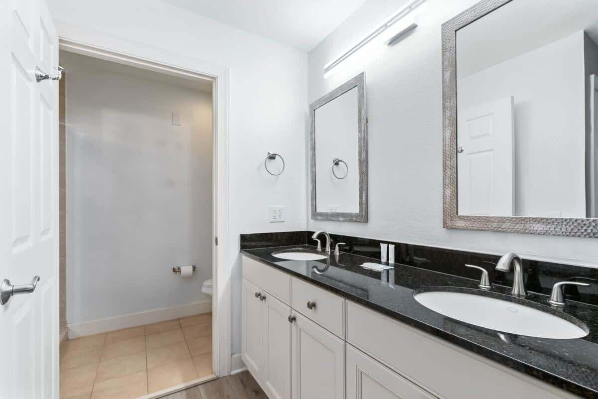 A bathroom with two sinks, a mirror, and a door leading to a shower.