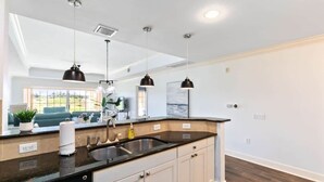 A modern kitchen with a black countertop, white cabinets, and pendant lighting. - Golf Course View Condo w/ Pool Access, Near Disney (Reunion)
